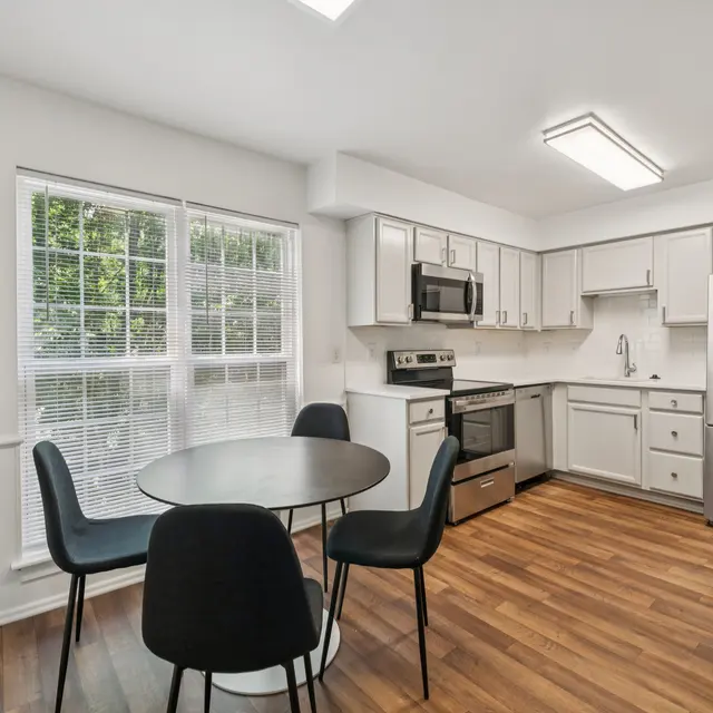 Bright Modern Kitchen A modern kitchen with a round table and black chairs, stainless steel appliances, and large windows providing natural light.