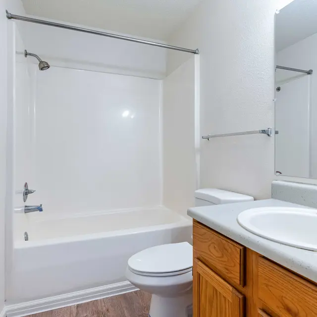 A clean and simple bathroom featuring a bathtub with a shower, a toilet, and a sink with wooden cabinetry.