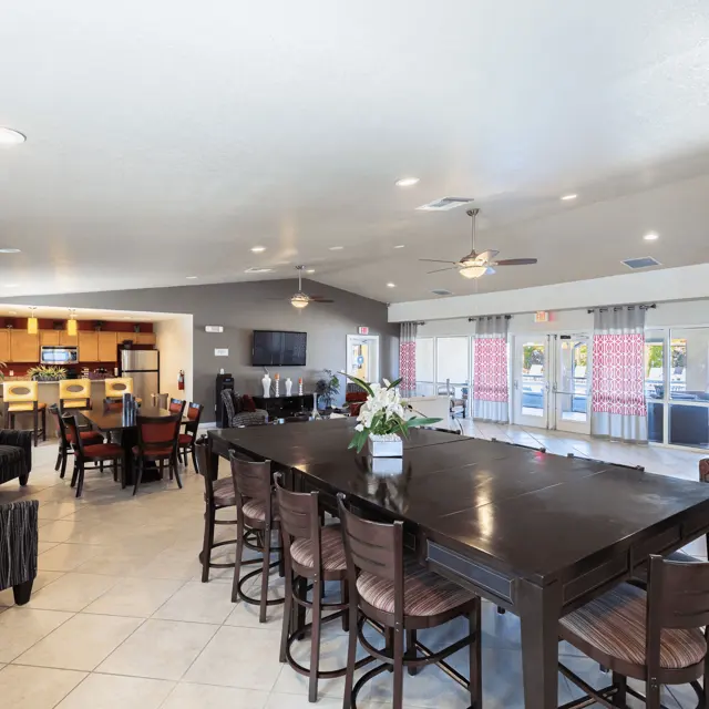 Spacious community room with dining area and kitchen, featuring large tables, seating, and bright windows.