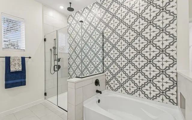 A modern bathroom featuring a stylish shower with glass doors, a freestanding bathtub, and a striking patterned tile wall in black and white.
