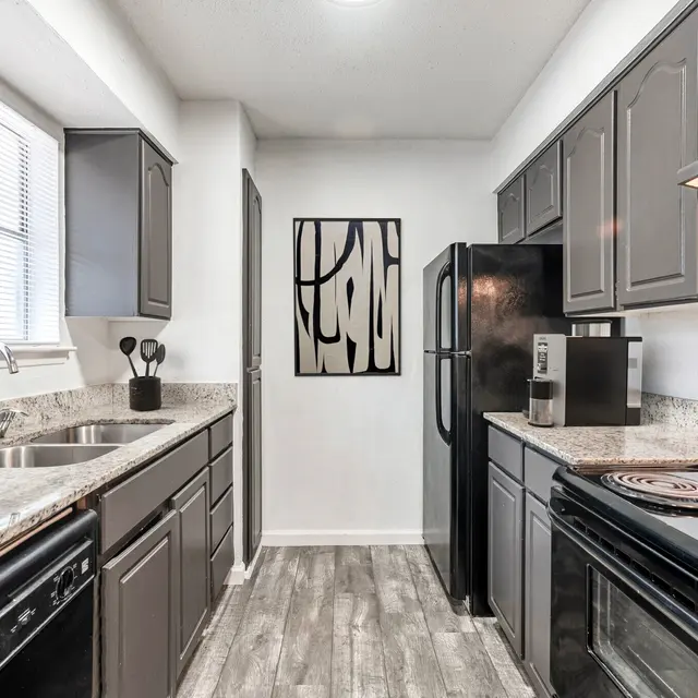 A modern kitchen featuring dark cabinets, granite countertops, and black appliances.
