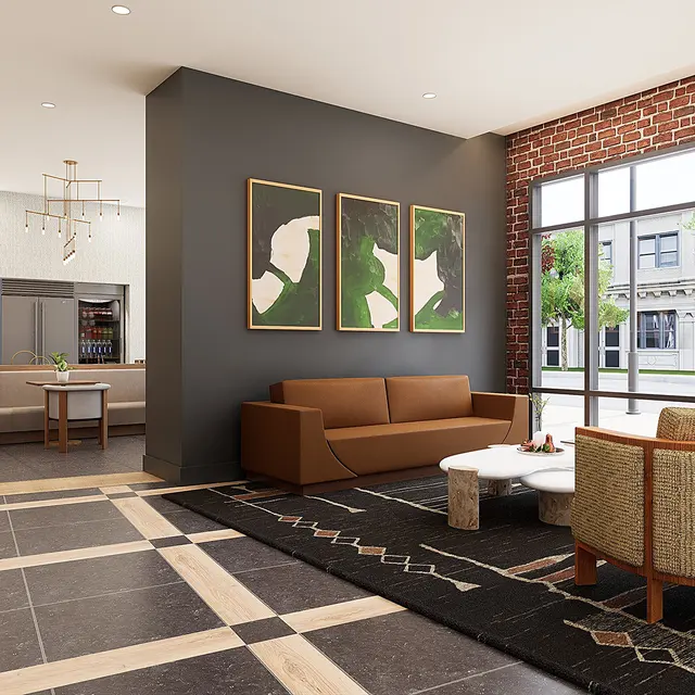 A stylish lobby space with a contemporary design featuring a mix of wooden furniture, framed artwork, and large windows. The area includes a seating arrangement with a sofa and armchairs, a coffee table, and a bar-like counter in the background.