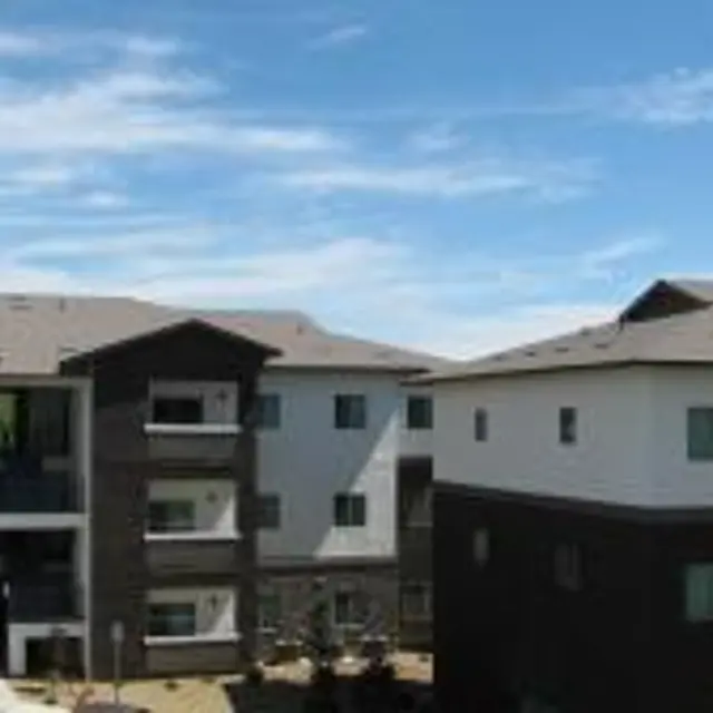 Modern residential apartment buildings with flat roofs and green landscaping under a partly cloudy sky.