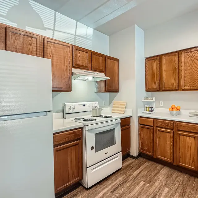 Modern Kitchen Interior A modern kitchen featuring wooden cabinets, a white refrigerator, a stove, and countertops with fruit on display.