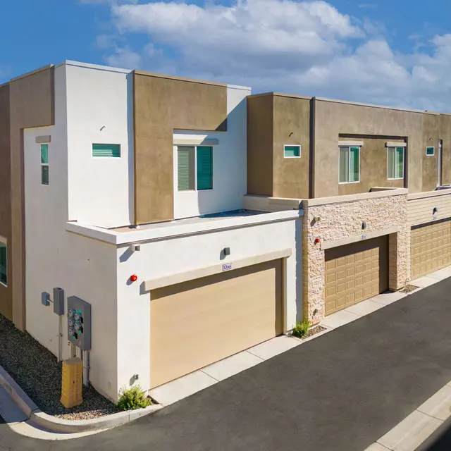 Modern Townhouses Architecture Aerial view of two modern townhouses with light-colored stucco and stone accents, featuring garages and large windows, under a blue sky with clouds.