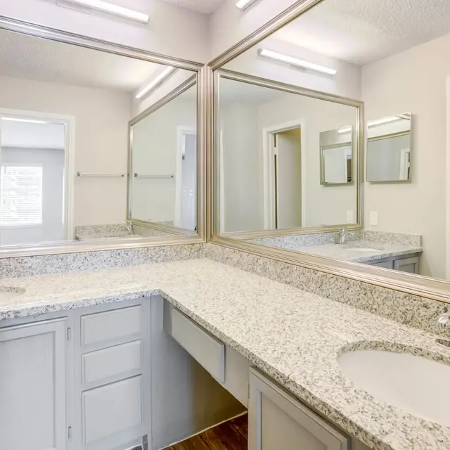 A well-lit modern bathroom featuring a dual sink vanity with granite countertops, large mirrors, and a spacious layout.