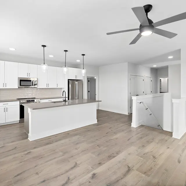 Modern Open Kitchen Interior A modern kitchen with an open layout, featuring white cabinets, a large central island, stainless steel appliances, and wooden flooring. The space is well-lit and includes a ceiling fan.