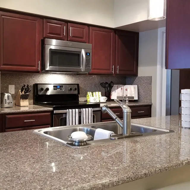 A modern kitchen featuring dark wood cabinets, a granite countertop, stainless steel appliances, and a sink with a faucet.