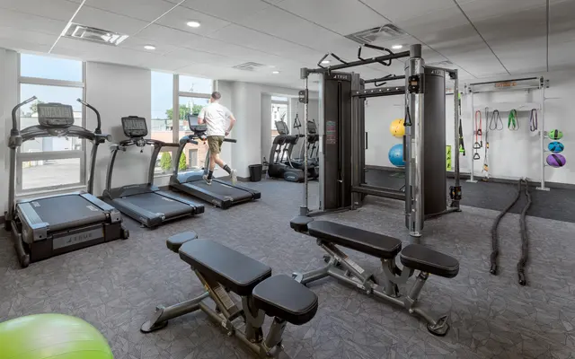 A modern gym with treadmills, an exercise bench, and a cable machine, with a person walking on a treadmill.
