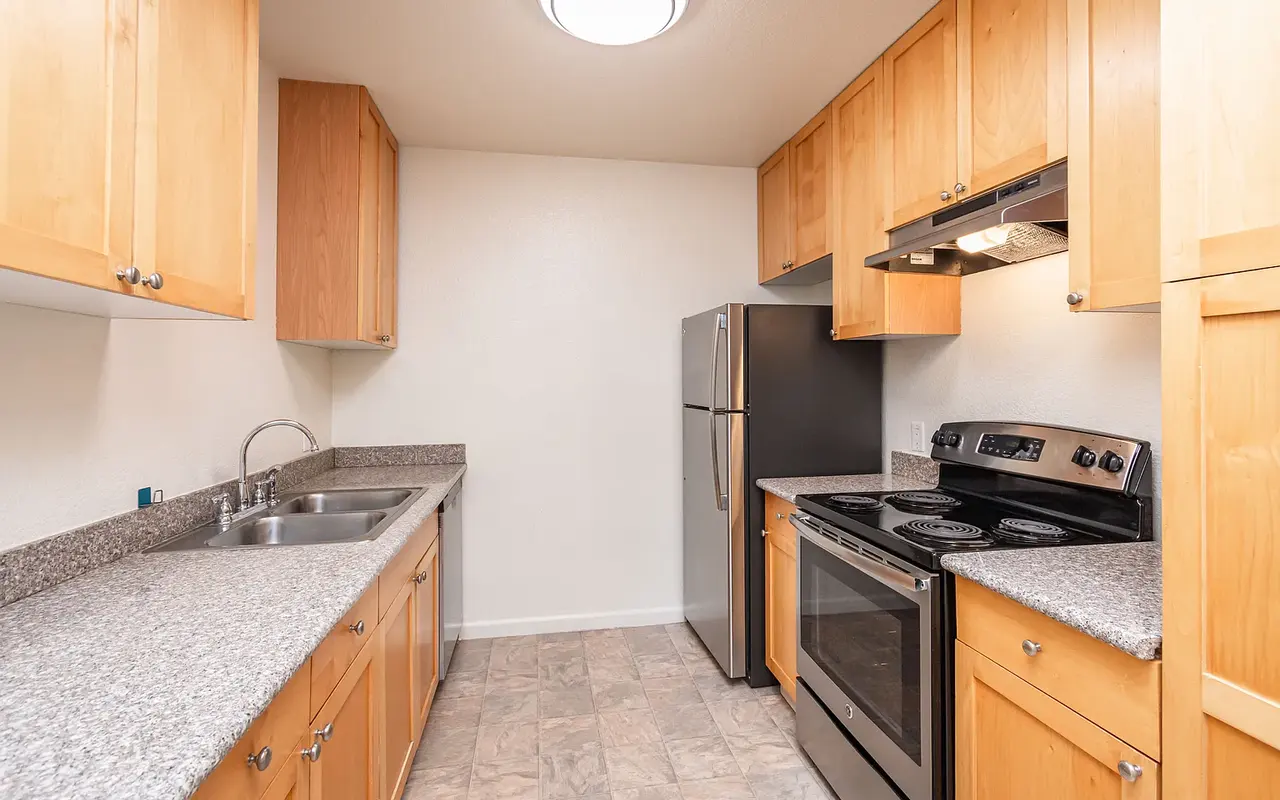 A modern kitchen featuring light wood cabinets, granite countertops, a stainless steel refrigerator, and an electric stove with an oven.
