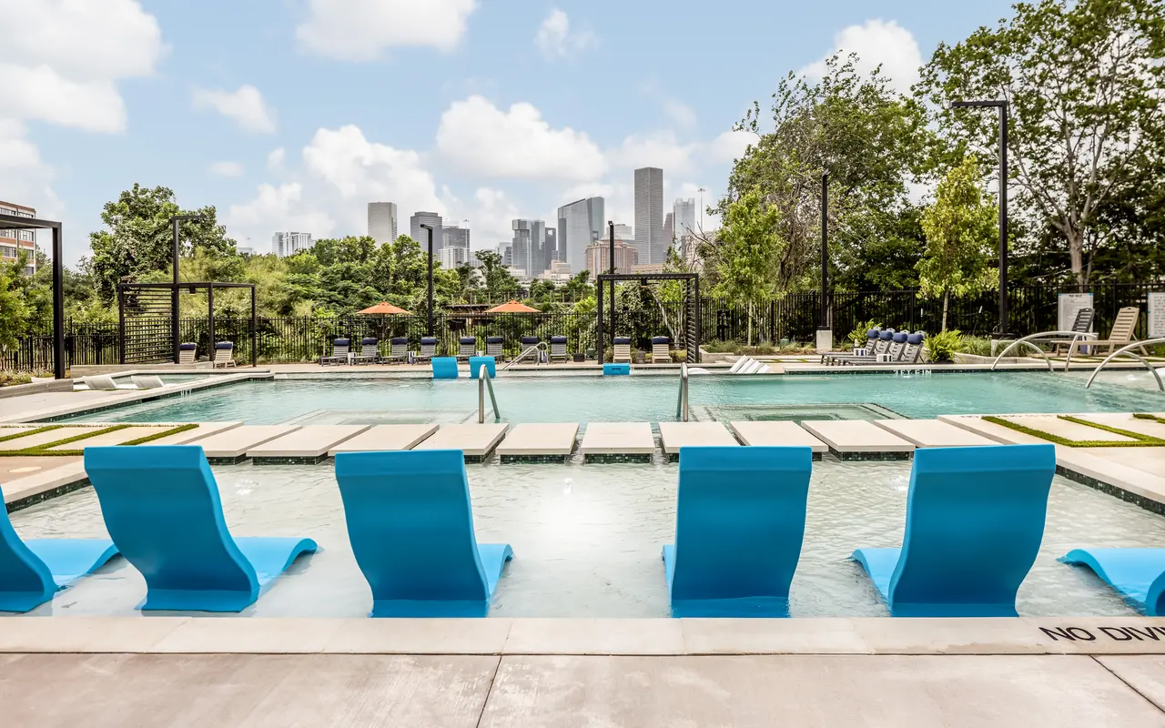Scenic pool view surrounded by trees with skyline backdrop and bright blue loungers.