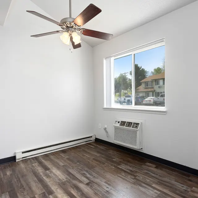 Bright Cozy Room with Ceiling Fan A small, bright room featuring a ceiling fan, a large window overlooking an outdoor view, and hardwood flooring.