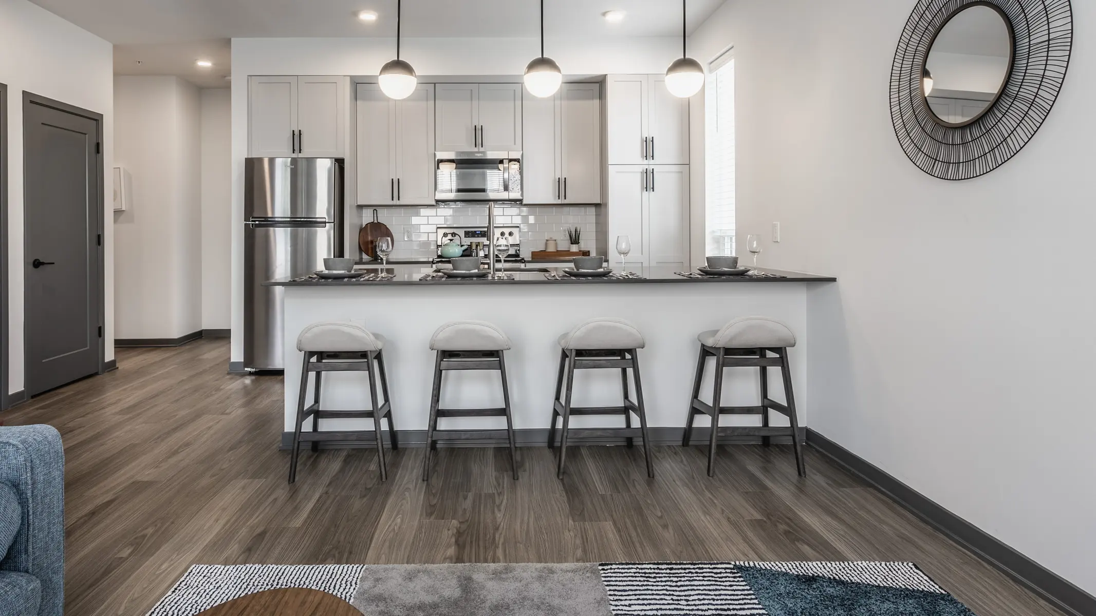 A modern kitchen featuring sleek cabinets, stainless steel appliances, and a bar area with stools, illuminated by pendant lights.