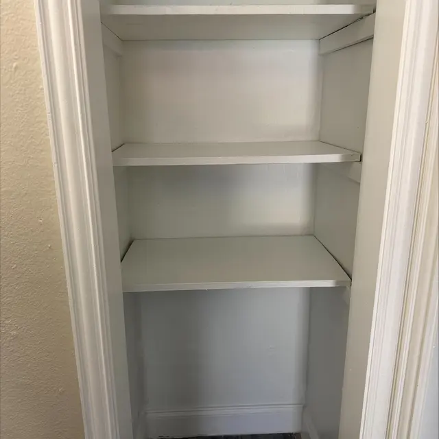 An empty closet with four white shelves against a light-colored wall.