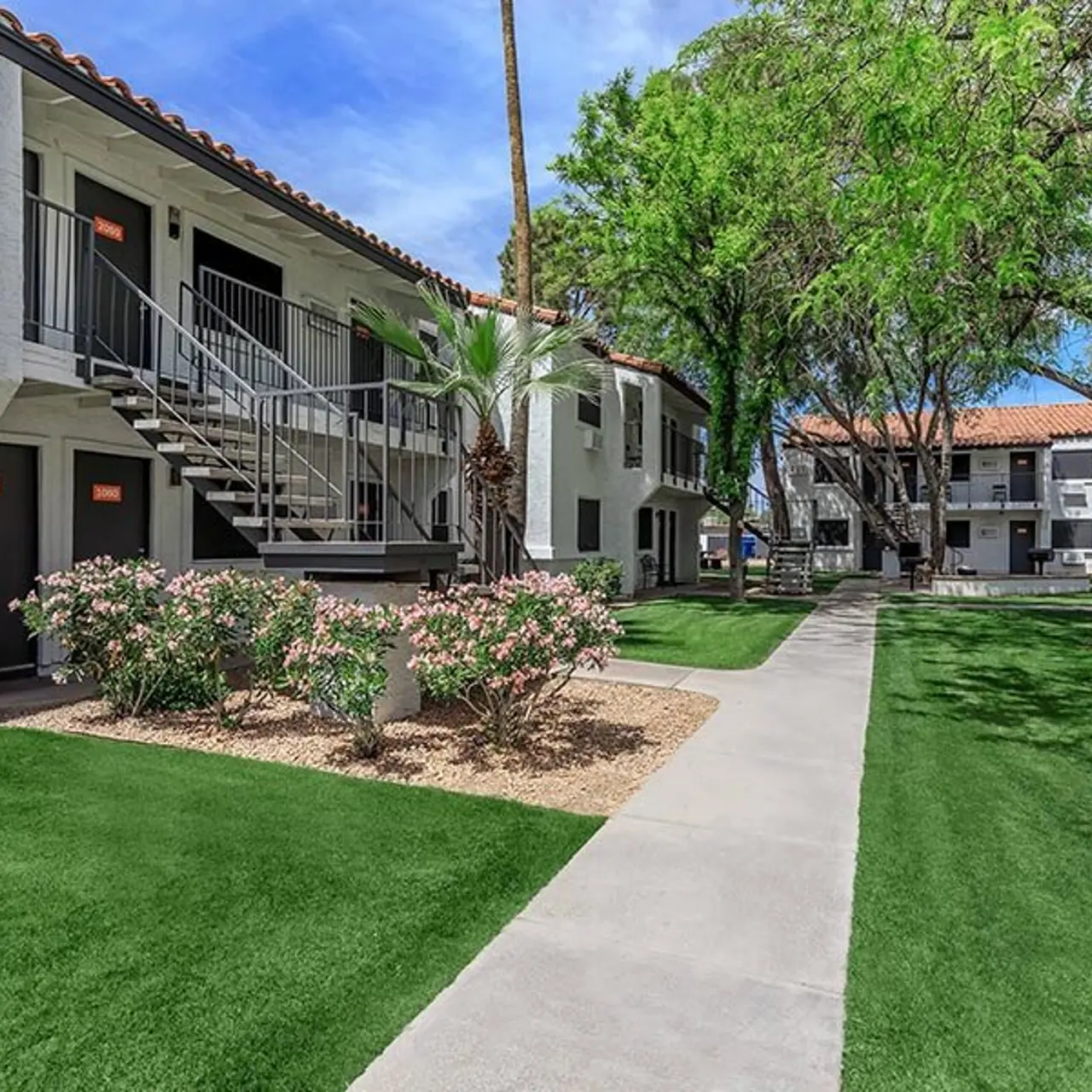 View of a landscaped apartment complex featuring two-story buildings, a walking path, and greenery.