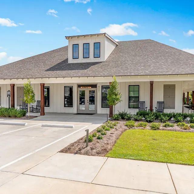Modern Residential Building A modern single-story residential building with a spacious exterior and manicured landscaping. The building features a flat roof, large front windows, and a welcoming porch area with rocking chairs.