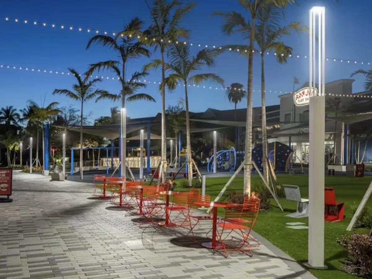 Vibrant Evening Community Space A well-lit community area at dusk featuring red chairs and palm trees, with playground equipment and a building in the background.