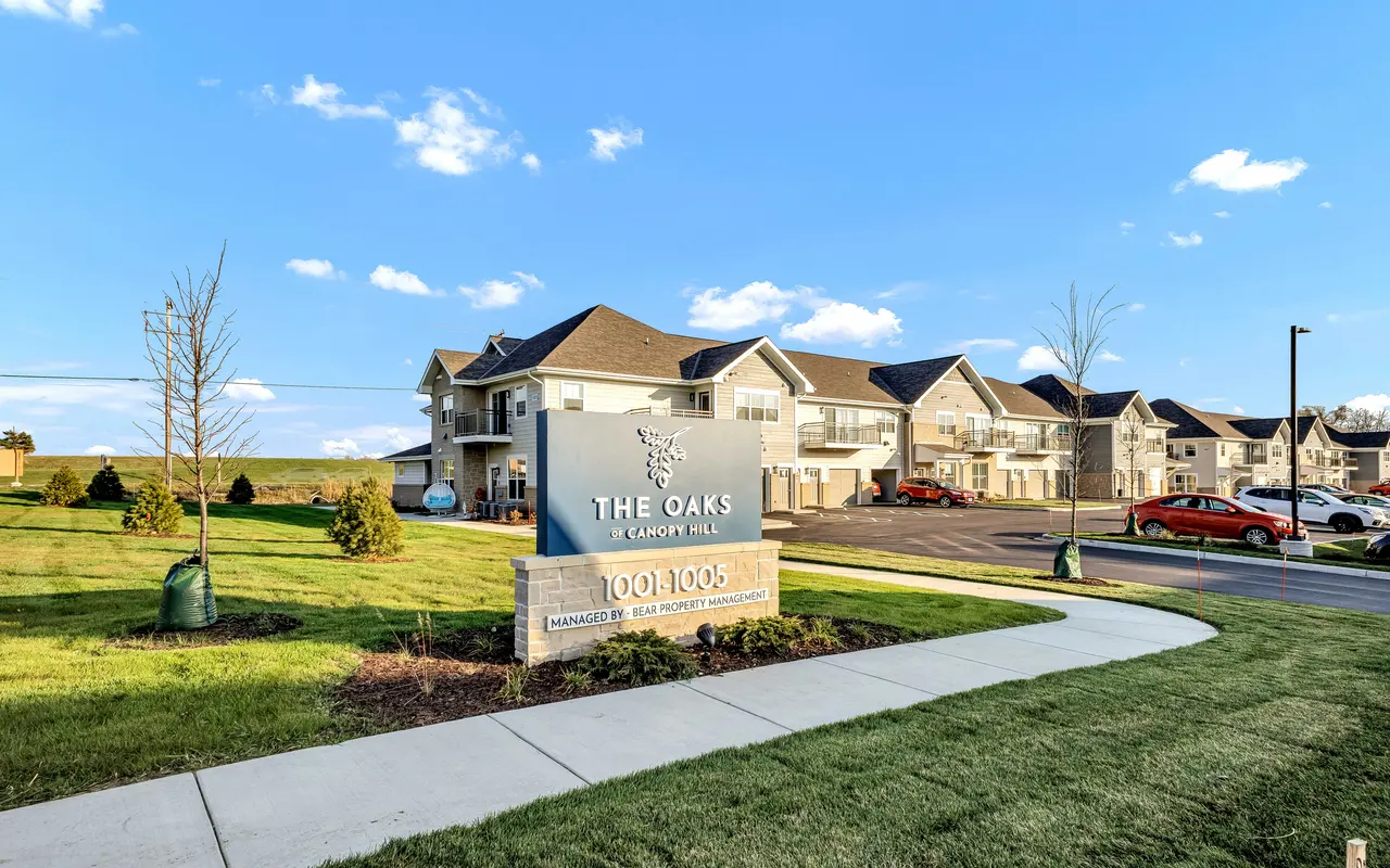 Exterior view of The Oaks at Canyon Hill apartment complex with a sign and landscaped area.