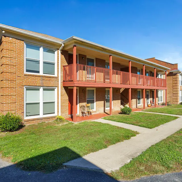 An exterior view of a two-story brick apartment complex with balconies and well-maintained lawns.