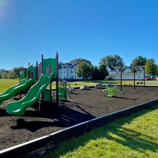 A playground featuring two green slides, swings, and various play equipment on a sunny day.