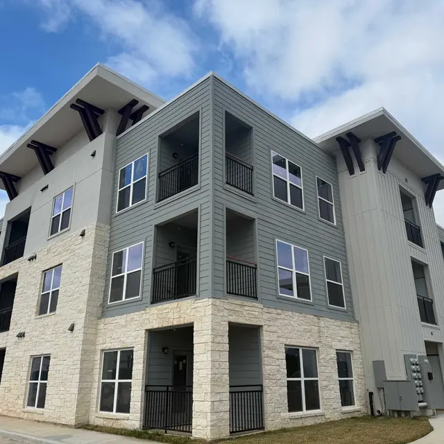 Exterior view of a modern apartment building featuring multiple balconies and a mix of stone and siding materials.