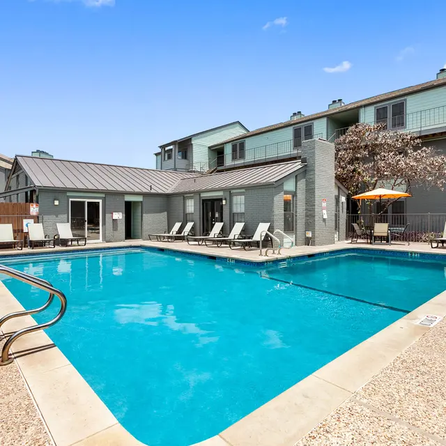 Apartment Pool Area A bright outdoor swimming pool area surrounded by lounge chairs and a building in the background.