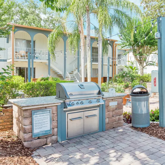 An outdoor grill area surrounded by greenery and apartment buildings in the background.