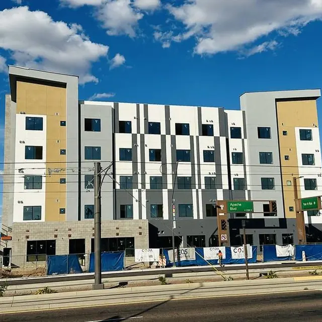 Newly constructed multi-story building under blue sky with fluffy clouds, featuring modern architectural design.