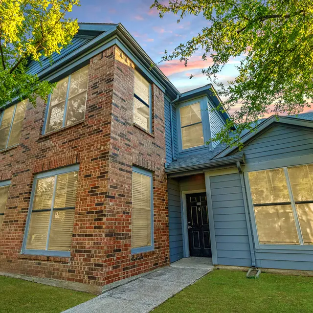 A modern brick house with large windows surrounded by greenery, showcasing a picturesque sky.