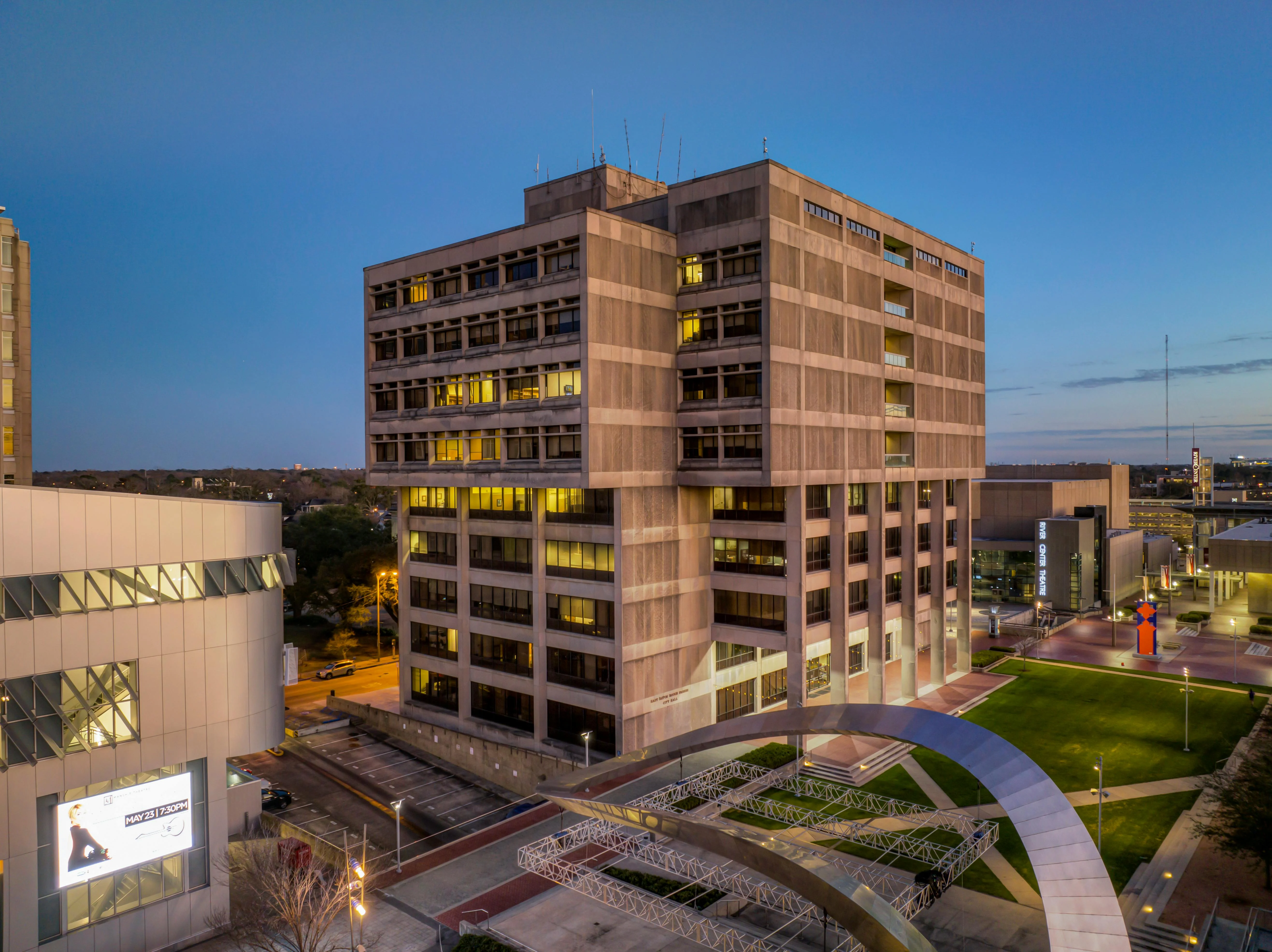 Modern Civic Building at Twilight A modern multi-story building with large windows and unique architectural design, situated near a nicely landscaped area during twilight.