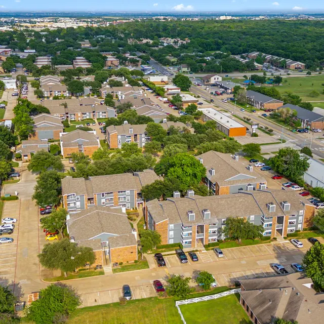 Aerial view of a residential area featuring multiple apartment buildings, parking spaces, and surrounding greenery.