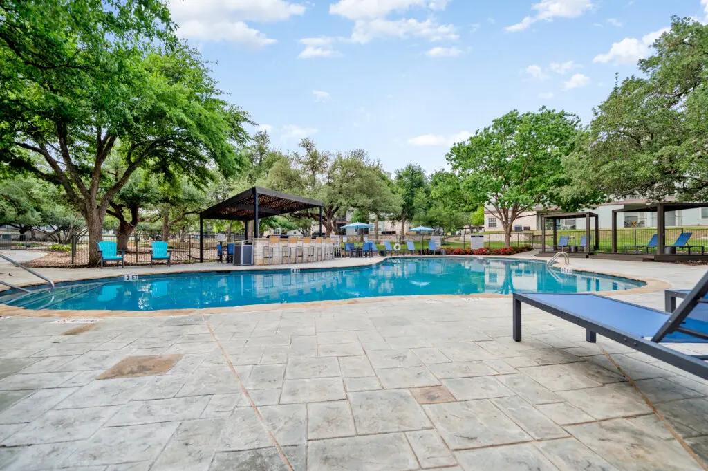 A swimming pool surrounded by trees and lounge chairs on a sunny day.