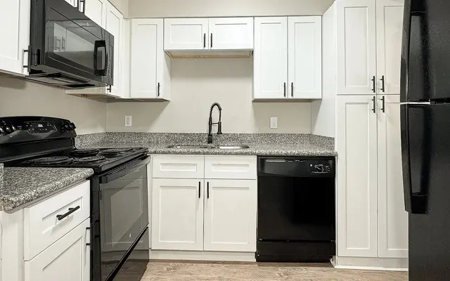 A modern kitchen featuring white cabinets, granite countertops, and black appliances including a stove, microwave, and refrigerator.