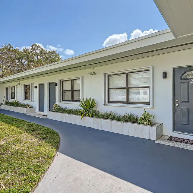 Exterior view of a modern apartment complex with a pathway leading to the doors and greenery in planters.