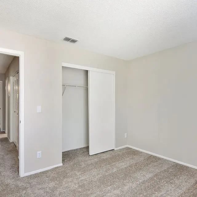 A bedroom with a closet and carpeted flooring, looking into a hallway.