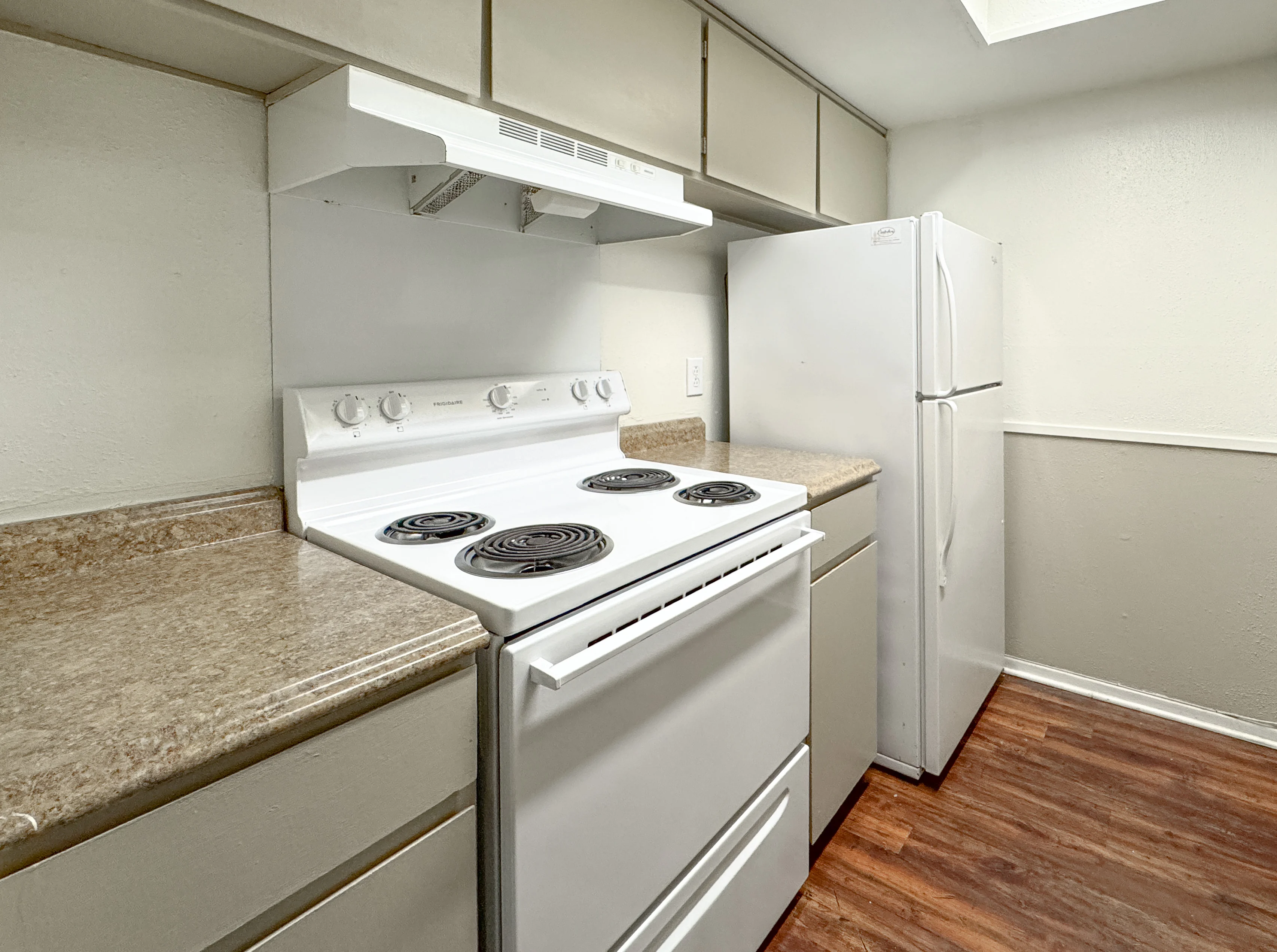 A small kitchen featuring a white stove with four burners, a white refrigerator, and light-colored cabinetry with a granite countertop.