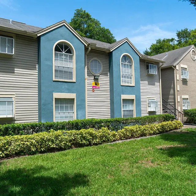 View of Bradenton Reserve's apartment buildings and walkway in between bushes and grass openings. 
