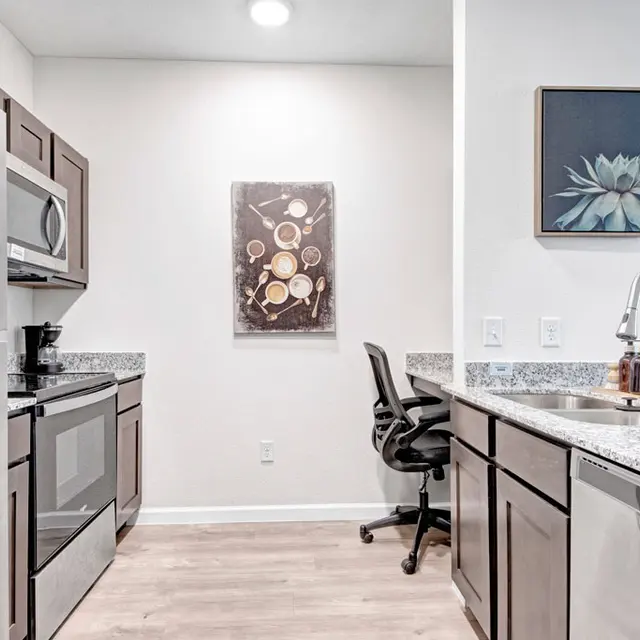 Modern Kitchen Interior A modern kitchen with stainless steel appliances, granite countertops, and wooden cabinets. There is a wall art piece and an office chair visible.