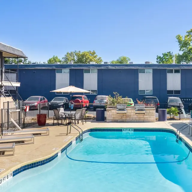 An outdoor pool area with lounge chairs and a surrounding apartment complex under a clear blue sky.