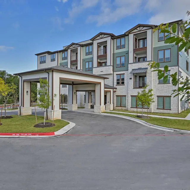 Modern apartment complex with multiple stories and a covered entrance, surrounded by landscaping.