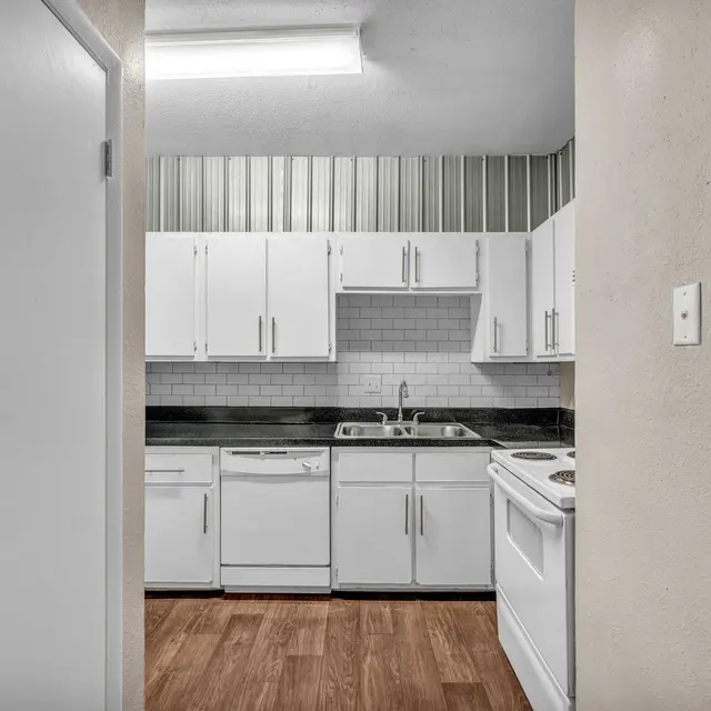 A hallway view leading a kitchen with hardwood-style flooring, white cabinets, and granite countertops.
