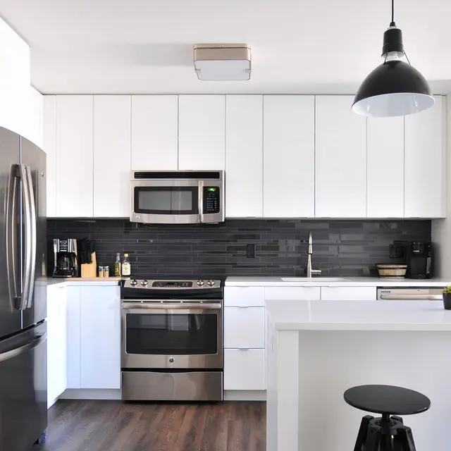 Modern kitchen with white cabinets, stainless steel appliances, black backsplash, dark wood floors, and two black pendant lights above an island.