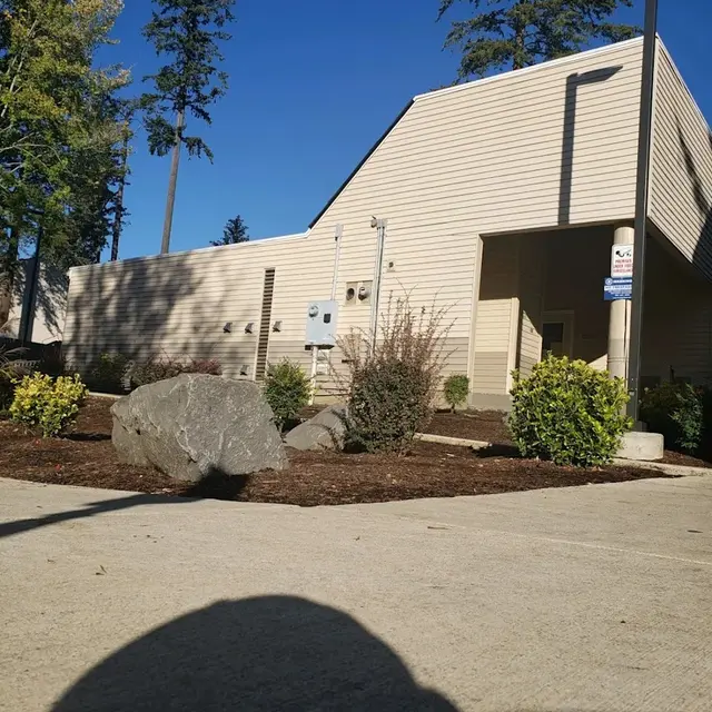 A beige-colored building surrounded by greenery and large rocks under a clear blue sky.