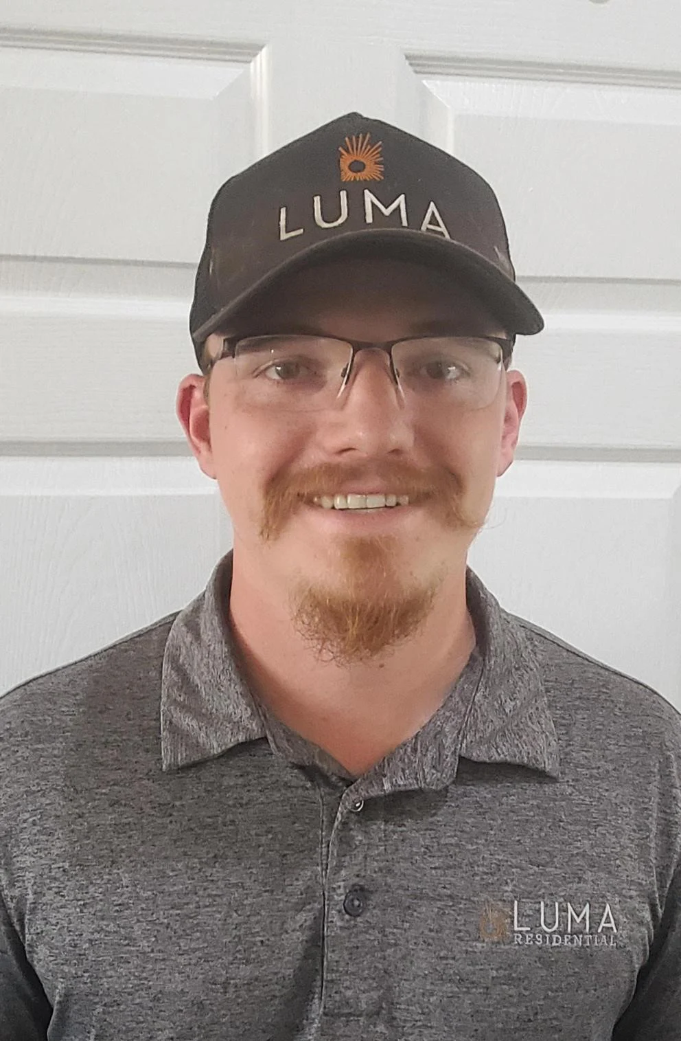 LUMA Residential Employee A smiling man wearing a grey polo shirt and a black cap with 'LUMA' text on it. He is standing in front of a white door.