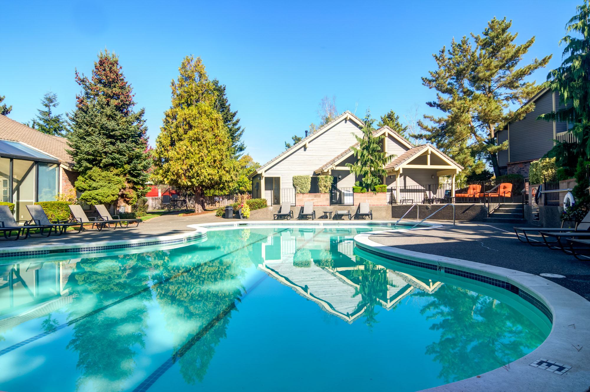 Serene Swimming Pool Area A clear swimming pool surrounded by lounge chairs and lush greenery, with residential buildings in the background under a clear blue sky.