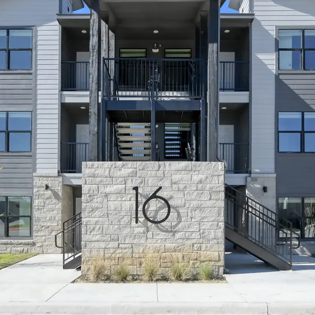 Exterior view of a modern apartment building featuring multiple units and a stone sign with the number 16.