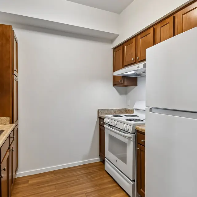 Compact Kitchen Design A compact kitchen featuring wooden cabinets, a white stove, and a white refrigerator. The countertops are light-colored with a sink visible on the left side.