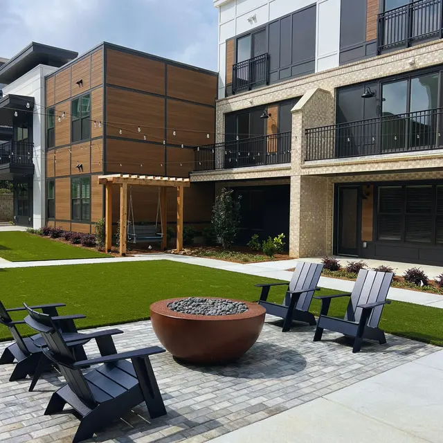 Outdoor Space at Modern Apartment Complex A modern apartment complex featuring a shared green space with chairs around a fire pit, pergola, and landscaped areas.