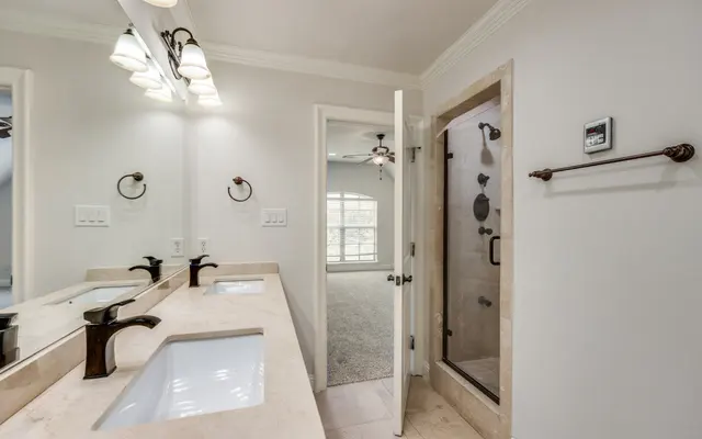 Elegant Modern Bathroom A modern bathroom featuring a double vanity with two sinks, decorative wall lights, and a shower enclosure. The space has light-colored walls and a door leading to another room.