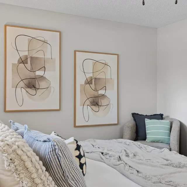 A cozy bedroom featuring two abstract art pieces on the wall, a light-colored bed with textured pillows, and a couch in the corner.